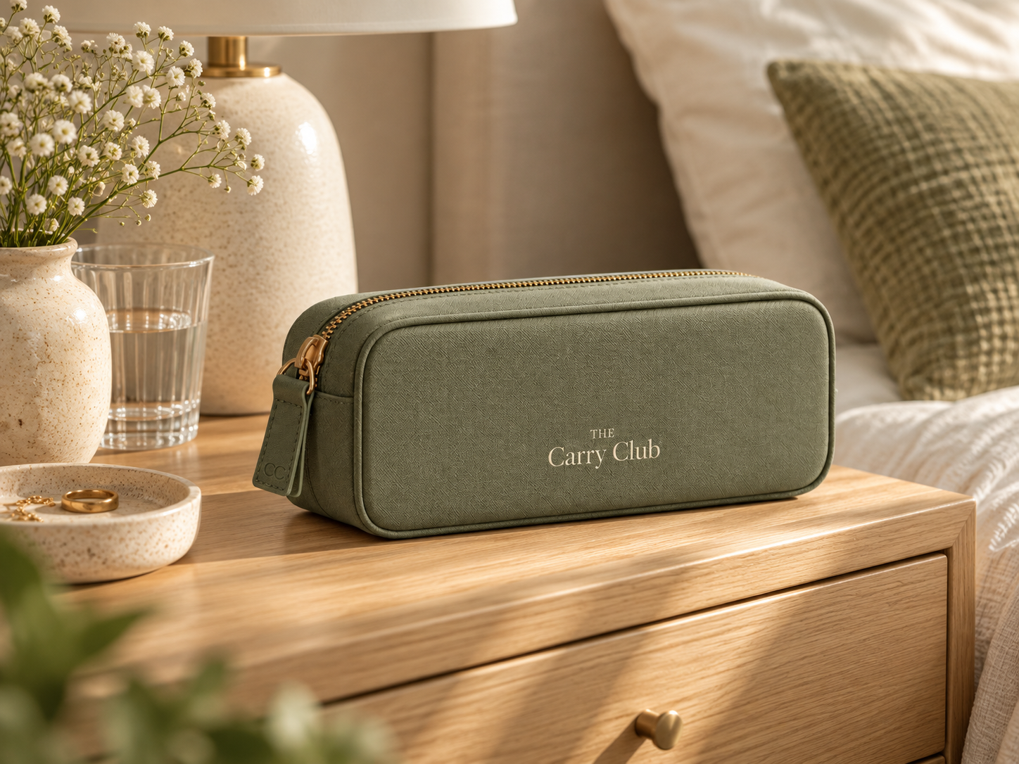 The Carry Club Sage Everyday Organiser on a wooden bedside table with a lamp, glass of water and flowers